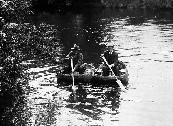 CORACLES. Two old men, paddling along a river in coracles. Date: 1930s