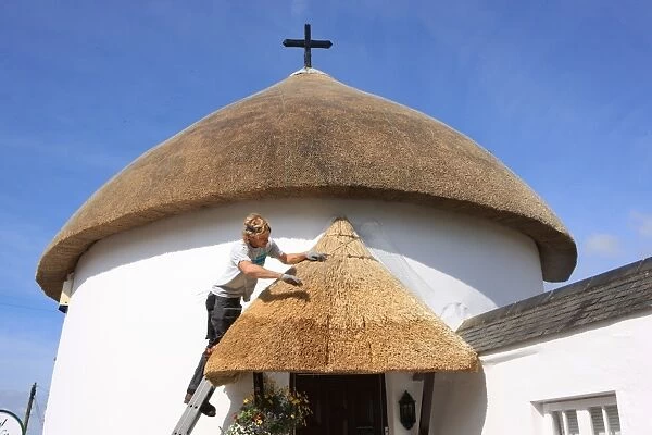 Thatching. A thatcher works on a round cottage in the village of Vergan Cornwall