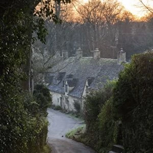 View down lane to Arlington Row Cotswold stone cottages at dawn, Bibury, Cotswolds