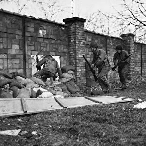A raiding party of soldiers from the 143rd Infantry Regiment, 36th Division, U. S. Seventh Army, dash through a sandbagged hole in a brick wall that opens onto the Moder River; the soldiers were raiding the enemy-held bank of the river opposite Haguenau, France, in order to bring back prisoners. Photographed 3 March 1945